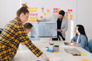 Four people in an office. They have post-it notes and computers as they are in a meeting.