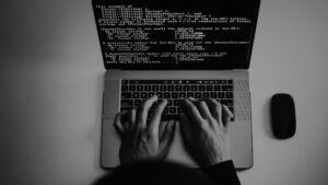 Hands typing on a laptop. The screen is filled with code.